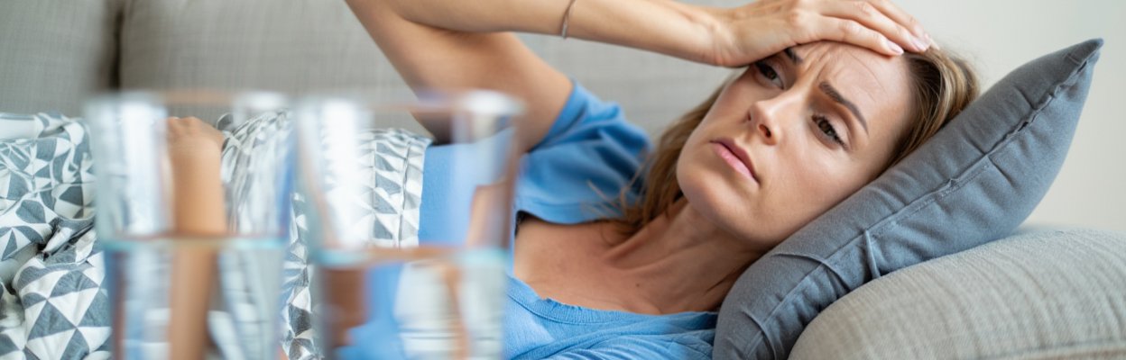 Женщина лежит на диване и держится за голову